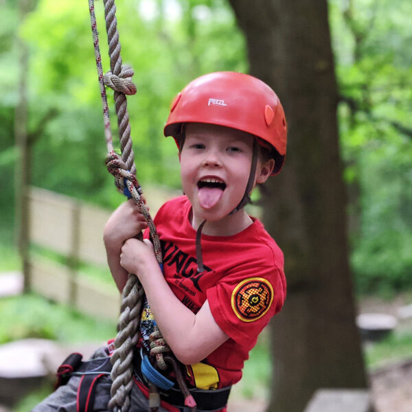 boy in red helmet sticking his tongue out on a rope