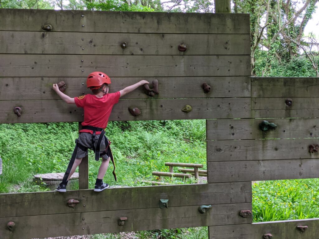 Child in a red tshirt climbing a small climbing wall.