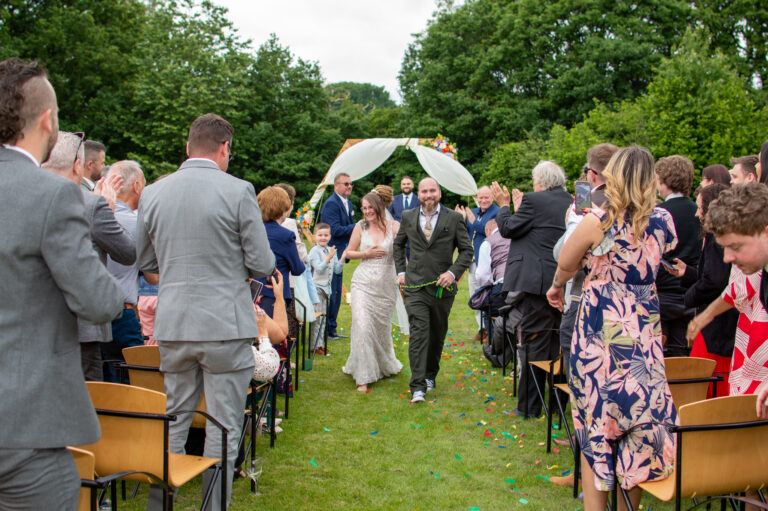 A bride and groom walking down the aisle smiling at guests